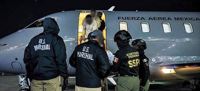 미 연방 요원 등이 죄수복을 입고 포승줄에 묶인 멕시코 마약 범죄 조직원들을 수송기를 통해 호송하고 있다. 이들은 시날로아 카르텔 등 멕시코 주요 마약 조직의 핵심 인사들이다./미 법무부