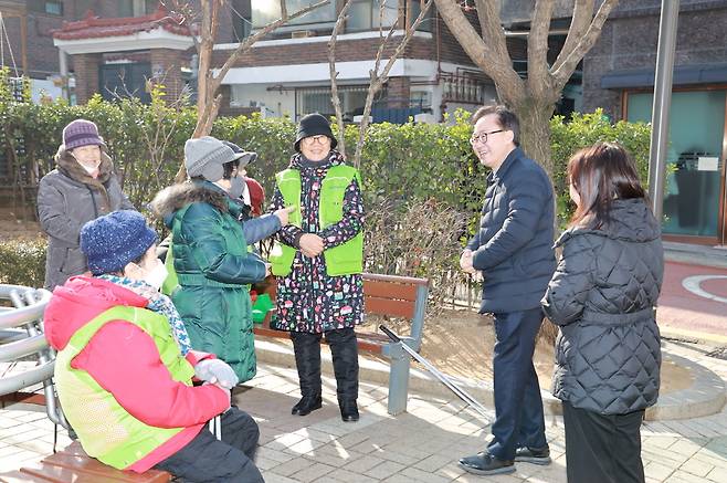 공원 벤치 주변에 유성훈 금천구청장을 포함한 여러 명이 서서 대화를 나누는 모습이다. 유성훈 구청장은 안경을 쓰고 미소를 지으며 대화에 참여하고 있다.