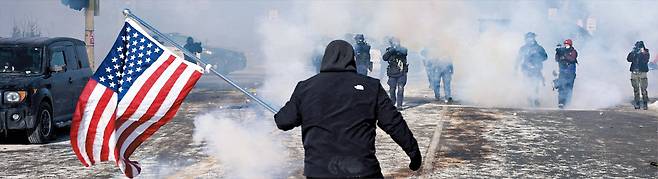 로이터 연합뉴스 미네소타 시위… 총구 앞에서도 놓지 못한 의지  24일 미국 미네소타주 미니애폴리스에서 강경 이민 단속에 항의하는 시위가 벌어진 가운데, 최루탄 연기 속에서 성조기를 든 한 남성이 무장한 연방 국경순찰대원들을 막아서고 있다. 이달 초 이민 단속 요원의 총격으로 37세 백인 여성이 숨진 데 이어, 이날 시위 진압 과정에서 백인 남성 알렉스 프레티(37)가 또다시 국경순찰대원의 총에 맞아 사망하면서 미 전역에서 이민 당국과 시민 사회 간 갈등이 고조되고 있다.