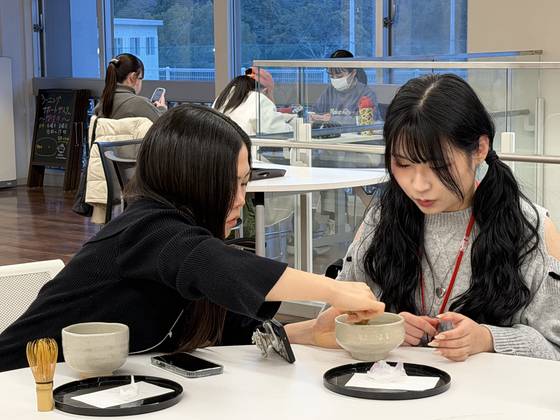 A Japanese student, left, helps a Korean student whisk matcha powder in a bowl during a cultural exchange session at Tezukayama Gakuin University in Osaka, Japan, on Jan. 22. [LEE SOO-JUNG]