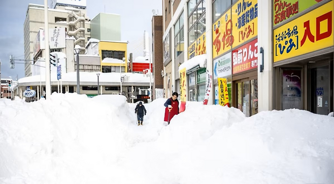 지난달 30일 일본 아오모리현 아오모리시의 한 가게 앞에서 직원이 눈을 치우고 있다. [AFP 뉴스1]