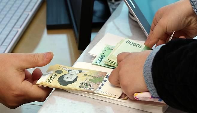A customer receives banknotes from a teller in a Hana Bank branch in Seocho District, southern Seoul, on Feb. 8, 2024. [NEWS1]