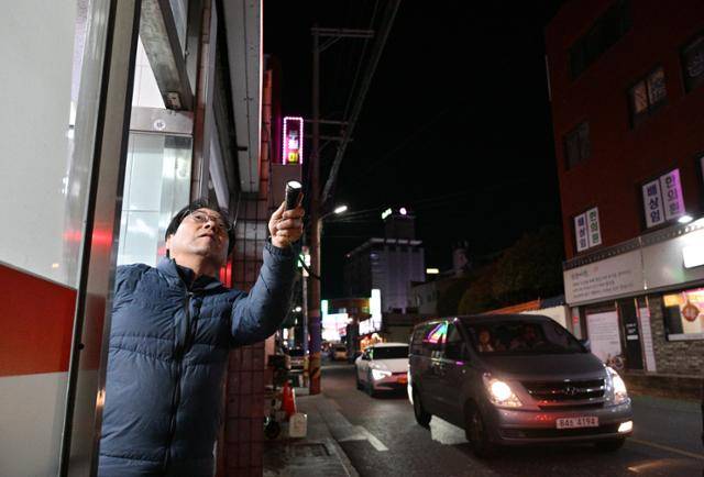 28일 경남 김해 부원동에서 가게를 운영 중인 주인이 손전등으로 비추며 가게 앞 떼까마귀를 쫓고 있다. 김해=최주연 기자
