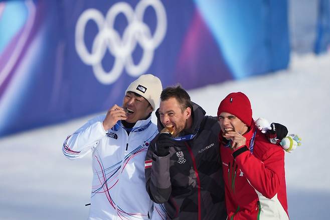 2026 밀라노.코르티나담페초 동계올림픽 스노보드 남자 평행대회전 시상식에서 메달리스트들이 메달을 깨무는 시늉을 하고 있다. 왼쪽부터 은메달의 한국 김상겸, 금메달의 오스트리아 벤자민 칼, 동메달의 불가리아 테르벨 잠피로프. 미국 NBC는 ″금메달(벤자민 칼)과 은메달(김상겸) 선수 나이를 합치면 77살″이라고 전했다. [AP=연합뉴스]