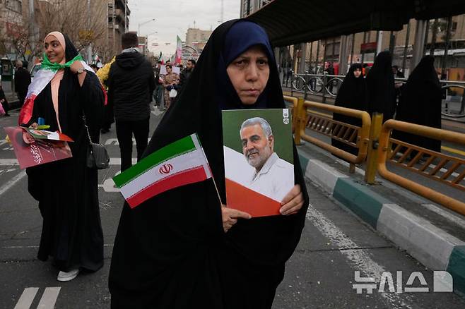 [테헤란=AP/뉴시스] 이란 이슬람 혁명 기념일인 11일 테헤란에서 한 여성이 이란 국기와 지난해 6월 이스파엘의 공습으로 숨진 혁명 수비대 장교의 사진을 들고 있다.2026.02.12.