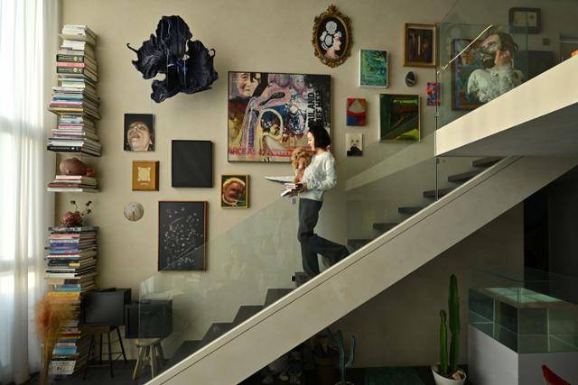이소영 작가가 복층 서재에서 반려견 '그림'이와 책을 안고 계단을 내려오고 있다. 벽에는 우한나, 조셉 예거, 맨디 엘사예, 코니 마이어, 올리버 비어, 제여란, 박경률 등의 작품이 걸려 있다. 미술품 360여 점을 소장하고 있는 그는 이 중 100여 점을 걸어 뒀다. 왼쪽 책탑에는 전시도록이 쌓여 있다. 강예진 기자