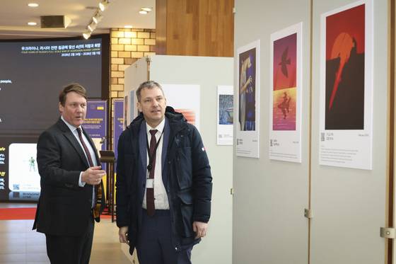 Deputy Head of the EU Delegation Roland Honekamp, left, and a visitor look at artworks depicting Russia’s brutal aggression against Ukraine at an exhibition at the Seocho District Office in southern Seoul on Feb. 24. [SEOCHO DISTRICT OFFICE]