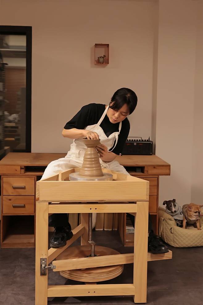 물레 작업을 하는 작가와 반려견 두 마리. "강아지들은 내 정체성"이라고 할 정도로 남다른 애정을 지닌 작가는 2022년 '개'를 모티브로 한 오브제와 찻주전자를 선보이기도 했다. /작가 제공