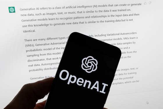 The OpenAI logo is displayed on a mobile phone in front of a computer screen with output from ChatGPT on March 21, 2023 in Boston. [AP/YONHAP]