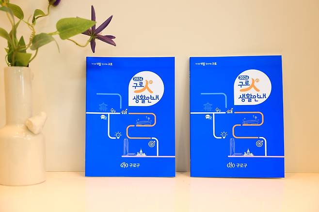 꽃병 옆에 ‘구로 생활안내’ 책자 두 권이 나란히 놓여 있는 사진이다. 책자 표지에는 제목: 구로구 생활 정보 ‘2026년 구로人(in) 생활안내’ 발간, 내용: 달라지는 제도·복지·민원 절차 등 생활정보 8개 주제로 정리... 지도·도표로 문화·체육·생활권 시설 쉽게 확인이 적혀 있다.