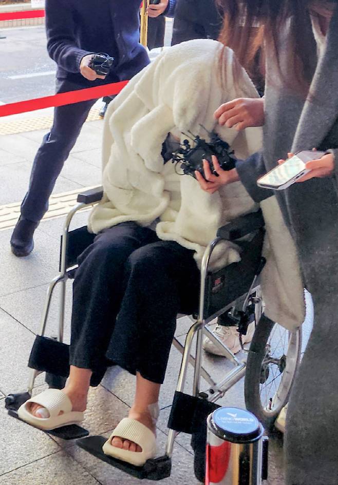 약에 취한 상태로 외제 SUV 차량을 몰고 반포대교를 달리다 한강 둔치로 추락한 운전자 A씨가 27일 서울 마포구 서부지방법원에서 열린 구속 전 피의자 심문(영장실질심사)에 옷으로 얼굴을 가리고 휠체어를 탄 채 출석하고 있다 (사진=연합뉴스)