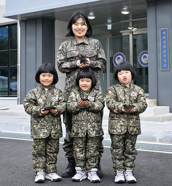 해군 제8전투훈련단 소속 이은주 상사와 세쌍둥이 딸들이 8전단 예하 예비전력관리전대 건물 앞에서 소아암 아동 돕기를 위해 자른 머리카락을 손에 들고 기념사진을 촬영하고 있다. [해군]