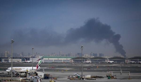 아랍에미리트(UAE) 두바이 국제공항이 지난 1일 폐쇄된 가운데 에미레이트 항공기들이 계류장에 세워져 있다. 그 뒤로 이란의 공격으로 발생한 연기 기둥이 피어오르고 있다. [출처=연합뉴스]
