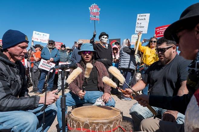 미국 뉴멕시코 산타페 인근 제프리 엡스타인의 ‘조로 목장’ 입구 근처에서 시위대가 드럼 연주단 ‘스위프트버드(Swiftbird)’의 공연에 맞춰 항의 시위를 벌이고 있다. 최근 목장 인근에 설치됐던 엡스타인 사건 피해자 추모물이 사라지면서 논란이 이어지고 있다. AFP 연합뉴스