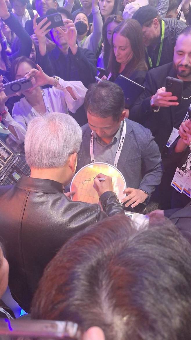 젠슨 황 엔비디아 최고경영자(CEO)가 16일(현지시간) 미국 캘리포니아 새너제이에서 열린 ‘GTC 2026’ 삼성전자 전시 부스에서 그록(Groq) AI LPU칩 파운드리 4나노 웨이퍼에 사인을 하고 있다. 삼성전자.