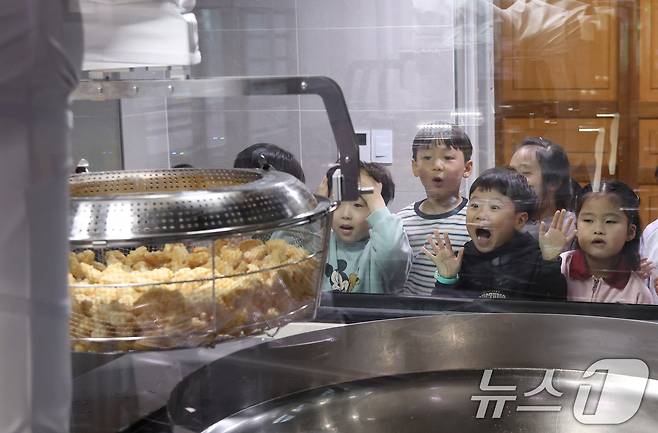 (수원=뉴스1) 김영운 기자 = 18일 경기 수원시 장안구 대평초등학교 내 위치한 거점형 학교급식 튀김 지원실에서 1학년 학생들이 튀김 조리 로봇이 직접 가동되는 현장을 보고 있다. 거점형 학교급식 튀김 지원실은 학생 선호도가 높은 튀김 식단을 별도 공간에서 최첨단 튀김 로봇을 도입해 공동으로 조리한 뒤 인근 학교에 제공하는 새로운 학교급식 모델이다. 2026.3.18 ⓒ 뉴스1 김영운 기자