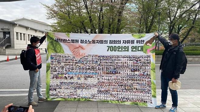 2022년 4월14일 공공운수노조 활동가들이 서울 서대문구 신촌 세브란스병원 앞에서 병원 청소노동자에 연대하는 700명의 목소리가 담긴 펼침막을 들어 보이고 있다. 공공운수노조 서울지부 제공