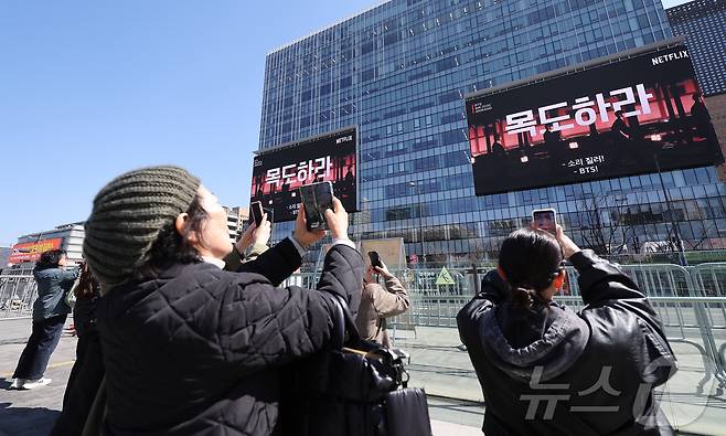 방탄소년단(BTS)의 서울 광화문광장 컴백 공연이 이틀 앞으로 다가온 19일 서울 종로구 광화문광장에서 외국인 팬들이 컴백 공연을 알리는 전광판 광고를 스마트폰으로 촬영하고 있다. 2026.3.19 ⓒ 뉴스1 김성진 기자