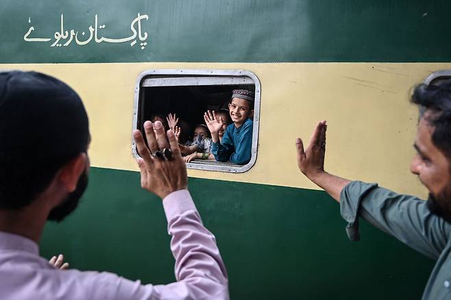 지난 18일 파키스탄 카라치의 한 기차역에서 이슬람 최대 명절 이드 알피트르를 앞두고 고향으로 향하는 열차에 탑승한 아이들이 플랫폼에 남은 가족들을 향해 손을 흔들고 있다. /AFP 연합뉴스