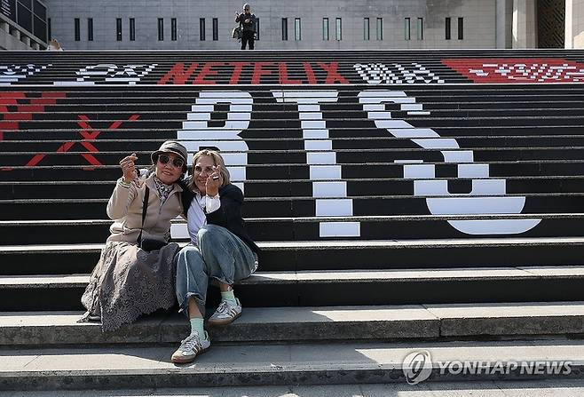 그룹 방탄소년단(BTS)의 광화문 공연을 앞둔 지난 19일 서울 종로구 세종문화회관 계단 BTS 홍모물 앞에서 외국인 관광객들이 기념사진을 찍고 있다. [연합뉴스]