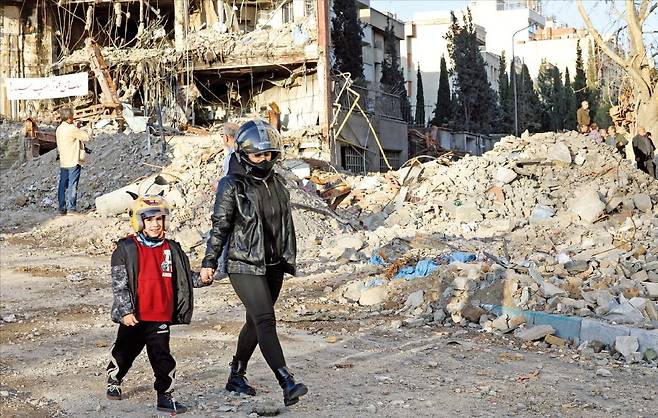 < 폭격 무서워…헬멧 쓴 아이 > 미국과 이스라엘의 이란 공습으로 시작된 이번 중동 전쟁은 4주 차에 접어들었다. 최근 미국·이스라엘의 폭격으로 파괴된 이란 테헤란 건물 잔해 옆을 헬멧을 쓴 어머니와 아들이 21일(현지시간) 지나가고 있다. 로이터연합뉴스