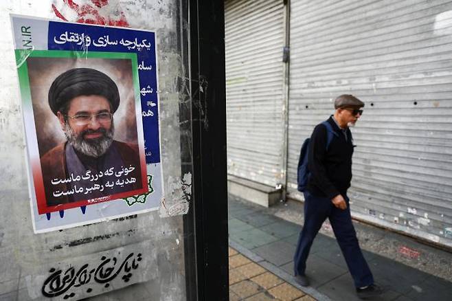26일 이란 최고 지도자 모즈타바 하메네이의 사진이 붙어 있는 테헤란 거리를 한 남성이 지나가고 있다. WANA로이터연합뉴스