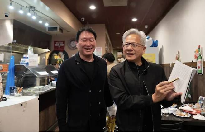 지난달 5일(현지 시각) 미국 캘리포니아 산타클라라의 한국식 호프집 '99치킨'에서 가진 최태원 SK그룹 회장과의 만찬회동에서 젠슨 황 엔비디아 최고경영자가 신간 '슈퍼모멘텀'을 펼쳐보이고 있다. / 연합뉴스