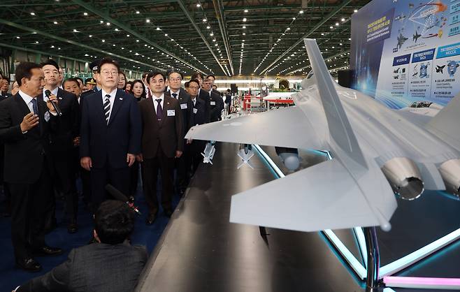 President Lee Jae Myung listens to a briefing on the KF-21 fighter jet at the production site from Korea Aerospace Industries CEO Kim Jong-chool following the rollout ceremony for the first mass-produced KF-21 at KAI in Sacheon, South Gyeongsang Province, on Wednesday. (Pool Photo via Yonhap)