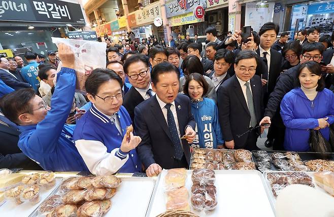 정청래 더불어민주당 대표(가운데)가 23일 오후 경남 양산시 중부동 양산남부시장에서 찹쌀도넛을 먹고 있다. 왼쪽은 김경수 경남지사 후보. 연합뉴스