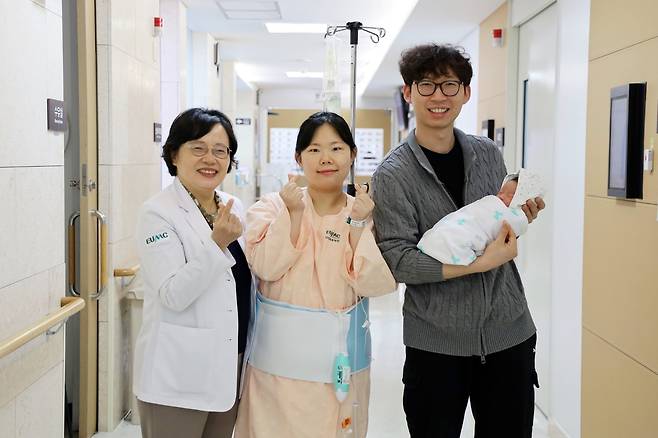 26년 전 자신을 받아준 김영주 교수(왼쪽)의 집도로 건강한 아들(오른쪽 아빠 품)을 출산한 산모 지선애 씨(가운데)가 입원실 복도에서 의료진과 함께 ‘손가락 하트’를 그리며 기념 촬영을 하고 있다. 이화의료원 제공