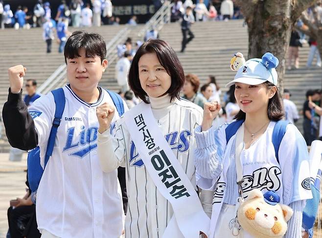 이진숙 전 방송통신위원장이 프로야구 개막일이던 지난 28일 대구 삼성라이온즈파크를 찾아 '대구시장 예비후보 이진숙'이라고 적힌 흰색 어깨띠를 두르고 시민들과 사진을 찍는 모습 ⓒ 페이스북 캡쳐
