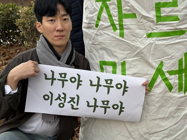 2026년 2월26일 서울 종로구 경희궁 서쪽, 18살 때 석면암 진단을 받고 16년째 투병 중인 이성진씨가 벌목 예정인 플라타너스 옆에서 펼침막을 들고 있다. 환경보건시민센터 제공