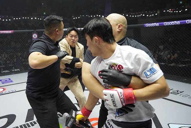 지난 해 12월 로드FC 075에서 정장 차림의 챔프 이정현이 조준건의 도발에격분해 케이지로 난입해 몸싸움을 벌이고 있다. 주위 심판들이 황급히 이를 뜯어말리고 있다.