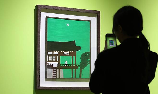 현대 판화사의 지평을 열고 고요와 멈춤을 한국적 화풍으로 시각화해온 김상유 작가 탄생 100주년 기념전 ‘쉽게 닳지 않는 사람’이 서울미술관에서 열리고 있다. 사진은 한 관람객이 김 작가의 ‘대산루’를 휴대폰 카메라로 담는 모습. 뉴시스
