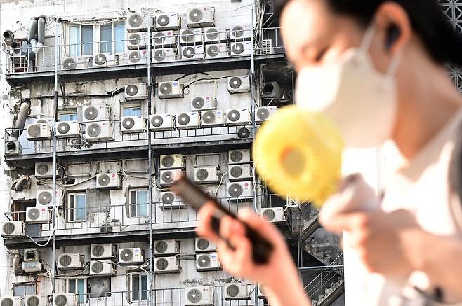 서울 중구 남대문 인근에 있는 건물 외벽에 줄지어 걸린 에어컨 실외기 앞을 지나가고 있다. 이상섭 기자
