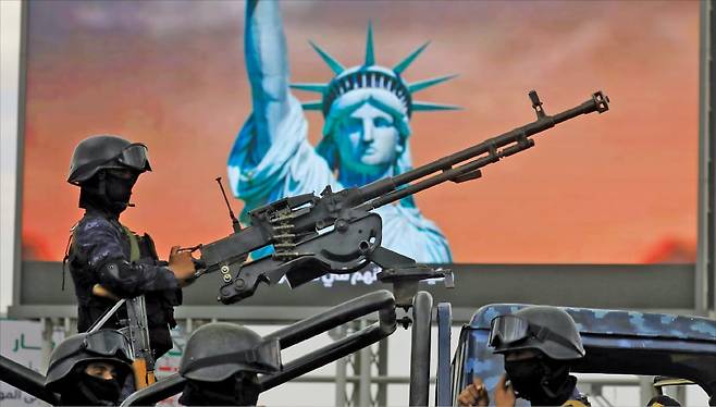 < 후티반군, 홍해 우회로 봉쇄 위협 > 이스라엘과 레바논 간 휴전이 발표된 지난 17일 예멘 사나에서 열린 헤즈볼라·레바논 연대 집회에서 후티반군 병사가 자유의 여신상이 표시된 디지털 광고판을 뒤로하고 기관총을 지키고 있다.  /EPA연합뉴스