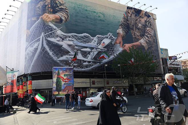 16일(현지시간) 이란 테헤란의 한 건물 앞을 시민들이 지나가고 있다. 건물 외벽에는 반미 선전물이 게시돼 있다. 2026.04.16 ⓒ 로이터=뉴스1