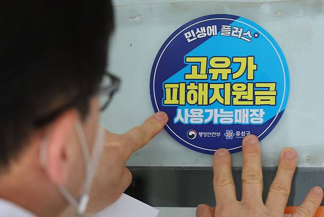 고유가 피해지원금 신청을 앞두고 23일 대전 유성구 한 식당 주인이 피해지원금 사용가능매장 안내문을 붙이고 있다. [뉴스1]