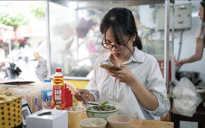 한 베트남 여성이 24일(현지시간) 이재명 대통령과 김혜경 여사가 전날 방문했던 하노이의 한 쌀국수집에서 사진을 찍고 있다. 사진=VN익스프레스 홈페이지 캡처