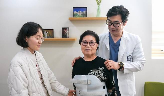 성영희 씨(가운데)는 네 번째 재수술 끝에 허리를 펴고 걸을 수 있게 됐다. 성 씨는 수술 전에는 딸 박주연 씨(왼쪽)의 도움 없이는 5m도 걸을 수 없는 상태였다. 수술을 집도한 조대진 강동경희대병원 신경외과 교수가 성 씨의 어깨를 펴면서 재활 훈련시 당부 사항을 알려주고 있다. 강동경희대병원 제공