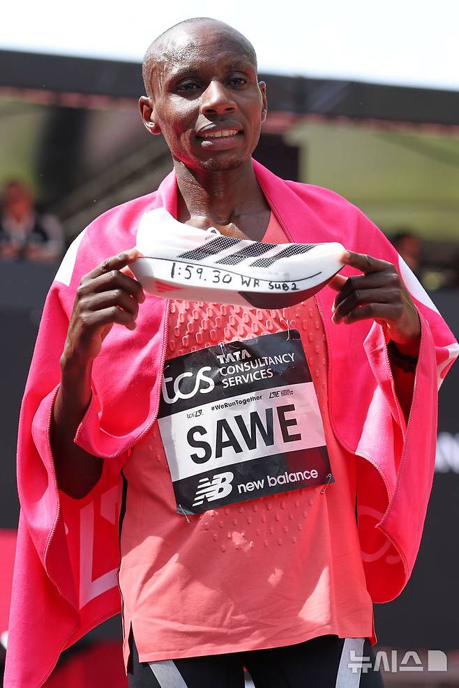 [런던=AP/뉴시스] 사바스티안 사웨(케냐)가 26일(현지 시간) 영국 런던에서 열린 2026 런던마라톤에서 1시간 59분 30초 세계신기록으로 결승선을 통과한 뒤 기록이 적힌 신발을 들고 포즈를 취하고 있다. 2026.04.26.
