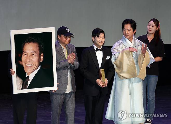 '아버지의 턱시도' (전주=연합뉴스) 나보배 기자 = 29일 전북 전주시 한국소리문화의전당 모악당에서 열린 제27회 전주국제영화제 개막식에서 조직위원회가 고 안성기 배우에게 특별공로상을 시상하고 있다. 이 상은 그의 아들 필립씨(왼쪽 두번째)가 참석해 대리 수상했다. 2026.4.29 warm@yna.co.kr
