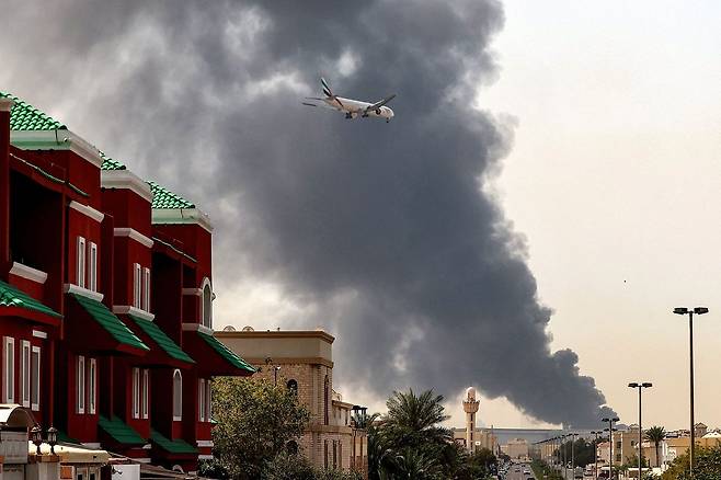 지난달 16일 아랍에미리트(UAE) 두바이 국제공항 인근이 이란의 공격으로 인한 폭발로 화염과 연기에 휩싸여 있는 가운데 에미레이트 항공 소속 비행기가 착륙을 준비하고 있다. AFP=연합뉴스