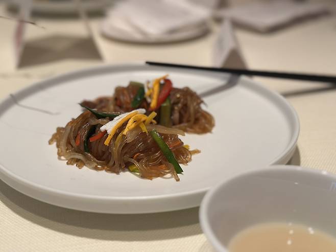 Stir-fried glass noodles with chives (center) paired with Jiran-jigyo Chamomile Makgeolli (Tammy Park/The Korea Herald)