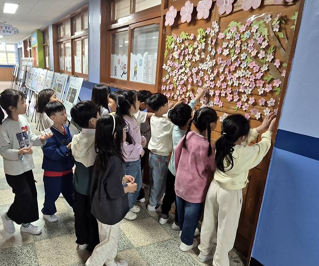 ▲&nbsp;수원동신초등학교 학생들이 독서 명언과 올해의 다짐을 담은 벚꽃 포스트잇을 붙이며 벚꽃 독서 나무를 완성하고 있다. /사진제공=수원동신초등학교