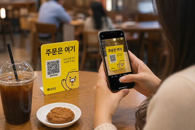 이용자가 카카오페이 ‘춘식이 QR’을 스마트폰으로 촬영해 테이블에서 메뉴 주문과 결제를 진행하고 있다. 해당 사진은 AI로 제작됨.