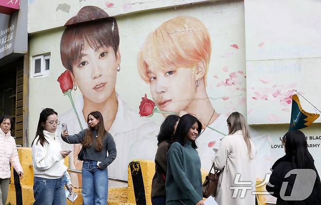 방탄소년단(BTS) 컴백 공연을 이틀 앞둔 19일 부산 서구 감천문화마을에서 외국인 관광객들이 부산이 고향인 BTS 멤버 정국·지민이 그려진 대형 벽화를 배경으로 기념촬영을 하고 있다. 2026.3.19 ⓒ 뉴스1 윤일지 기자