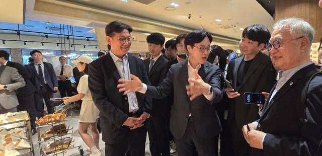 김정관(사진 가운데) 산업통상부 장관과 임영진 로쏘 성심당 대표가 27일 대전 롯데백화점 성심당 대전점에서 AI 로봇이 적용된 튀김소보로 생산 공정을 살펴보고 있다. [산업통상부 공동취재단]