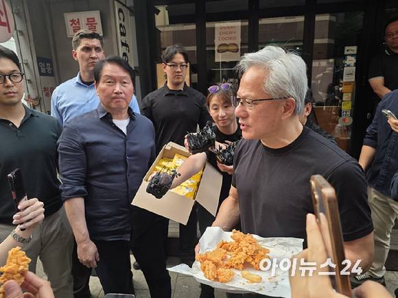 젠슨 황 엔비디아 최고경영자(CEO)가 7일 서울 강남구 삼성동 깐부치킨 앞에서 시민들과 취재진에게 후라이드치킨을 나눠주고 있다. 왼쪽 뒤편에는 SK하이닉스의 HBM 과자가 담긴 상자가 보인다. [사진=박지은 기자]