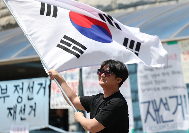 6·3 지방선거 투표용지 부족 사태를 규탄하며 재선거를 요구하는 ‘잠실 개표소 봉쇄 시위’가 계속되고 있는 9일 서울 송파구 올림픽공원 핸드볼경기장에서 한 참가자가 태극기를 흔들고 있다. [연합뉴스]
